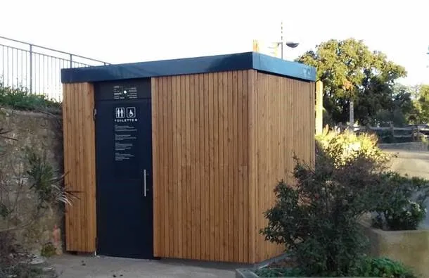 Öffentliche Toiletten mit Holzfassade, umgeben von Büschen