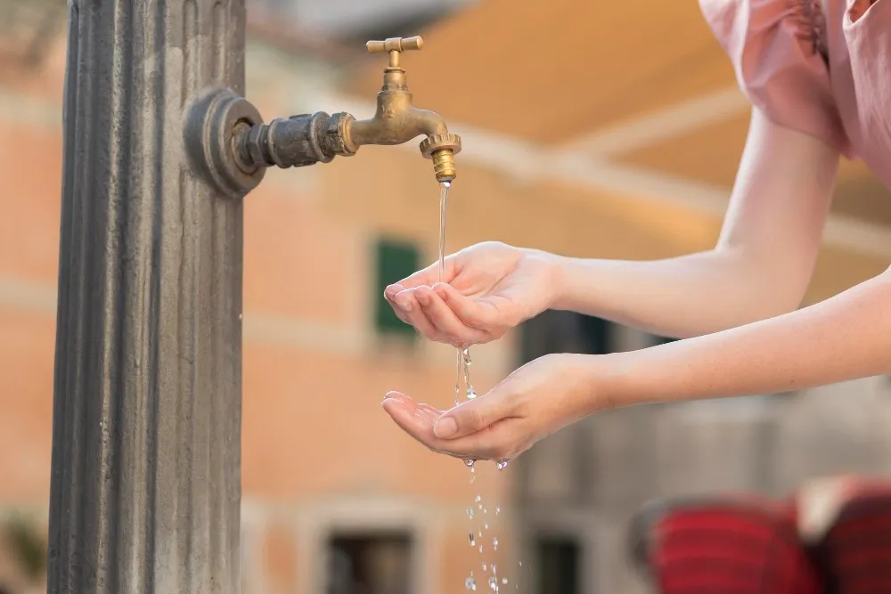 Frau, die an einem Brunnen Wasser trinkt.