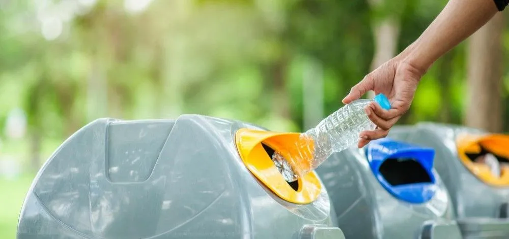 Person, die eine Flasche in einen Mülleimer wirft