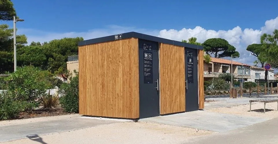 Dubbele grijze en houten sanitaire voorzieningen aan de rand van het zand